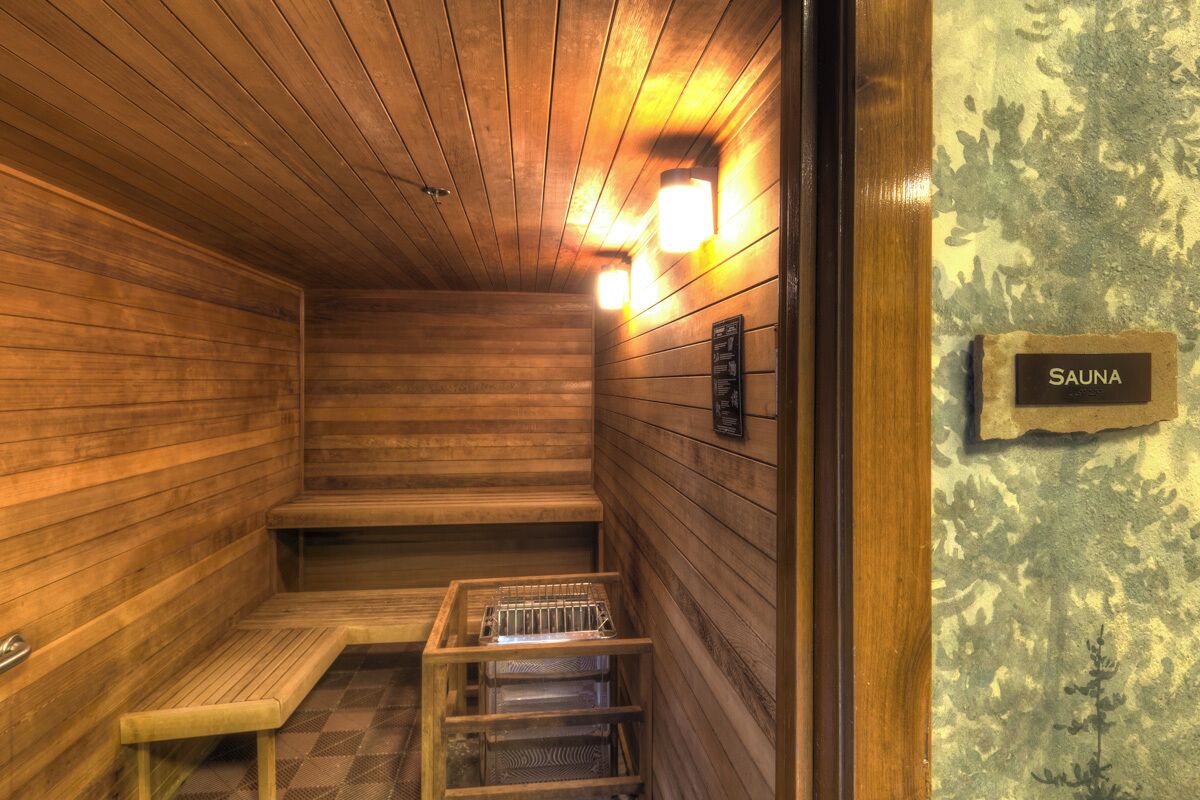 A sauna with wooden walls and benches, a tiled floor, and a sign labeled "SAUNA".
