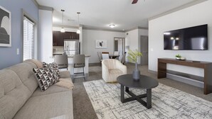 Ein modernes Wohnzimmer mit einer Couch, einem Couchtisch, einem Fernseher und einem Essbereich mit Stühlen und einem Tisch.
