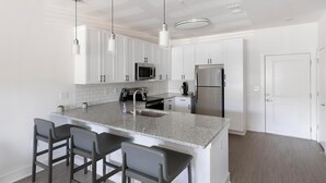 A modern kitchen with white cabinets, a granite countertop, stainless steel appliances, and pendant lighting. - Landing | Chic 1BD, Pool, Gym (Athens)