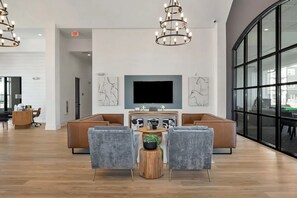 A modern lounge area with a large sofa, two armchairs, a coffee table, and a TV mounted on the wall.