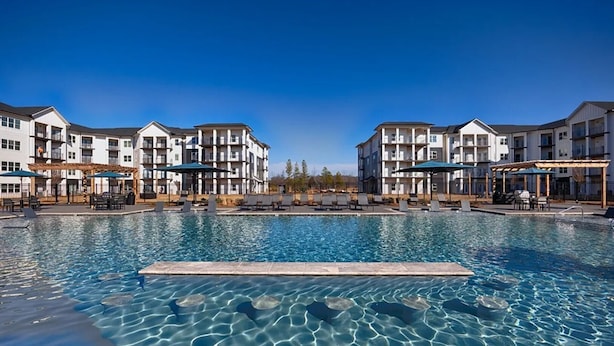 Une piscine entourée de bâtiments à plusieurs étages dotés de balcons, avec des chaises longues et des parasols à proximité.