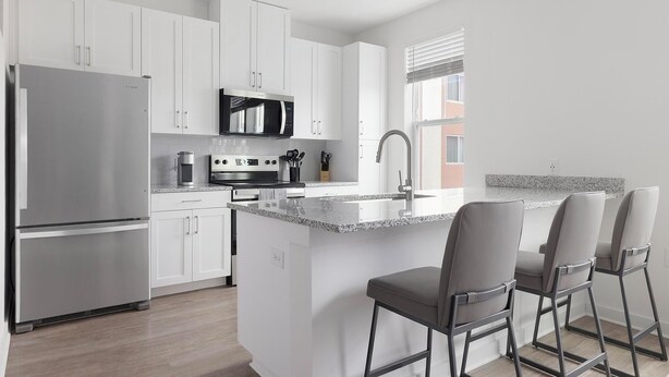 Una cocina moderna con armarios blancos, electrodomésticos de acero inoxidable, encimera de granito y una zona de asientos con taburetes de bar.