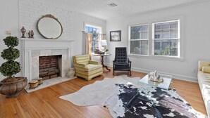 A living room with a fireplace, a large mirror, a leather sofa, and a glass coffee table. - Adorable 2-bedroom cottage in midtown Tulsa with a dreamy weeping willow. (Tulsa)