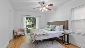 A bedroom with a bed, a ceiling fan, a small table, and a view of the outdoors. - Adorable 2-bedroom cottage in midtown Tulsa with a dreamy weeping willow. (Tulsa)