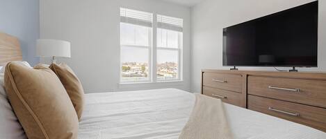 A bedroom with a bed, a TV, a window, and a view of a parking lot.