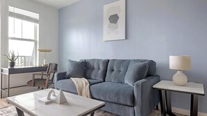 Ein Wohnzimmer mit grauem Sofa, einem kleinen Tisch, einer Lampe und einem Topfpflanzen.