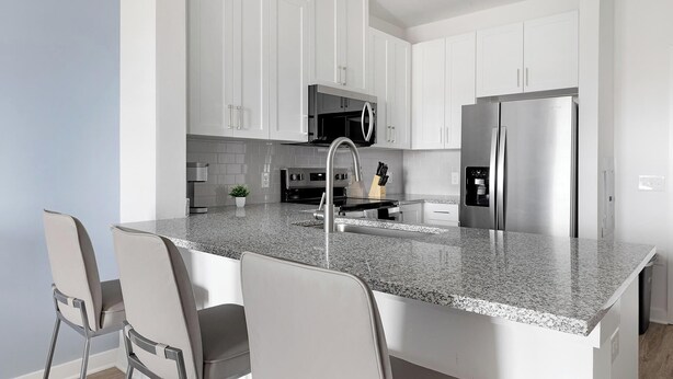 Eine moderne Küche mit weißen Schränken, einem Edelstahl-Kühlschrank, einer eingebauten Mikrowelle und einer Arbeitsplatte aus Granit.