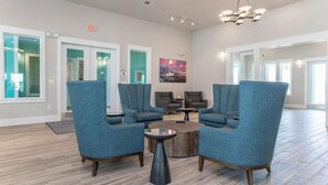 A lobby with blue armchairs, a round coffee table, and a painting on the wall. - Landing | Spectacular 1BD, Gym, Clubhouse (Rockport)