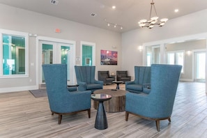 A lobby with blue armchairs, a round coffee table, and a painting on the wall. - Landing | Incredible 1BD, Gym, Clubhouse (Rockport)