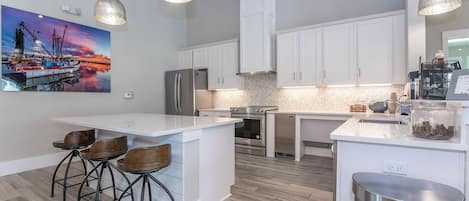 A modern kitchen with white cabinetry, a central island with bar stools, stainless steel appliances, and pendant lighting.