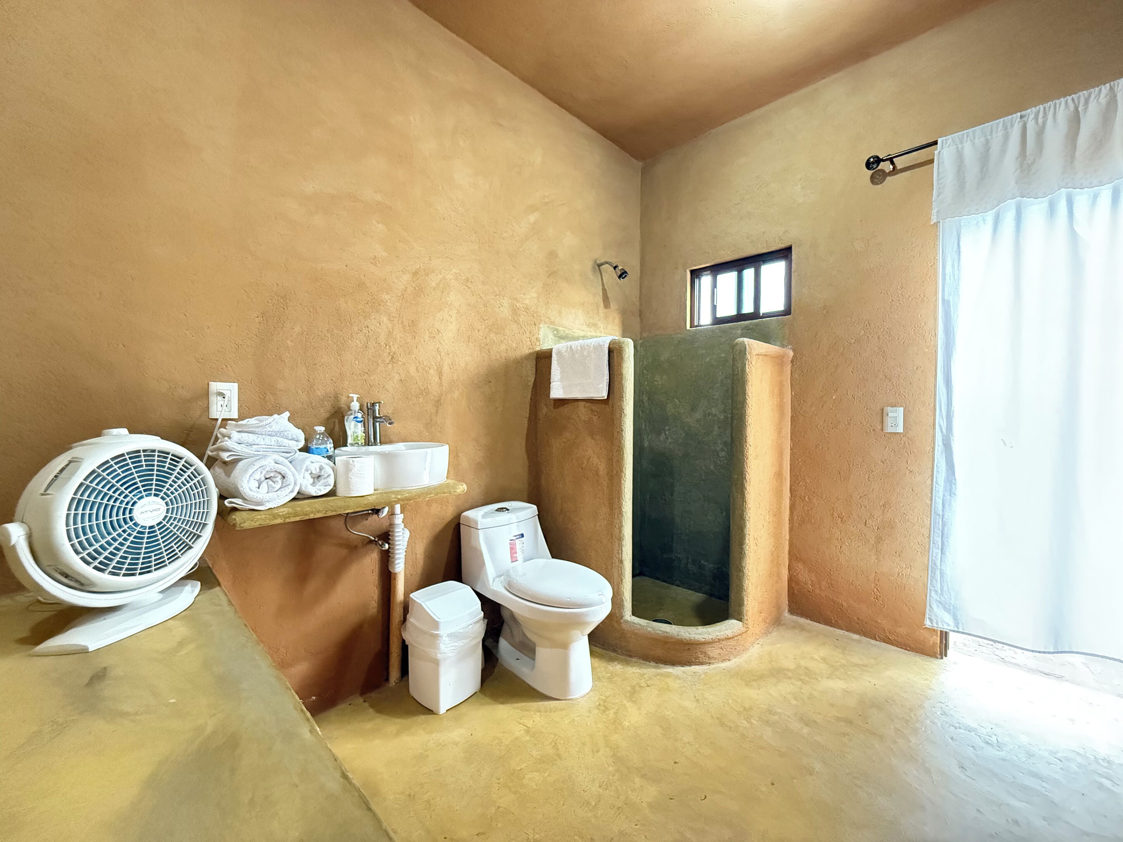 Baño con inodoro, lavamanos, ventilador y zona de ducha.