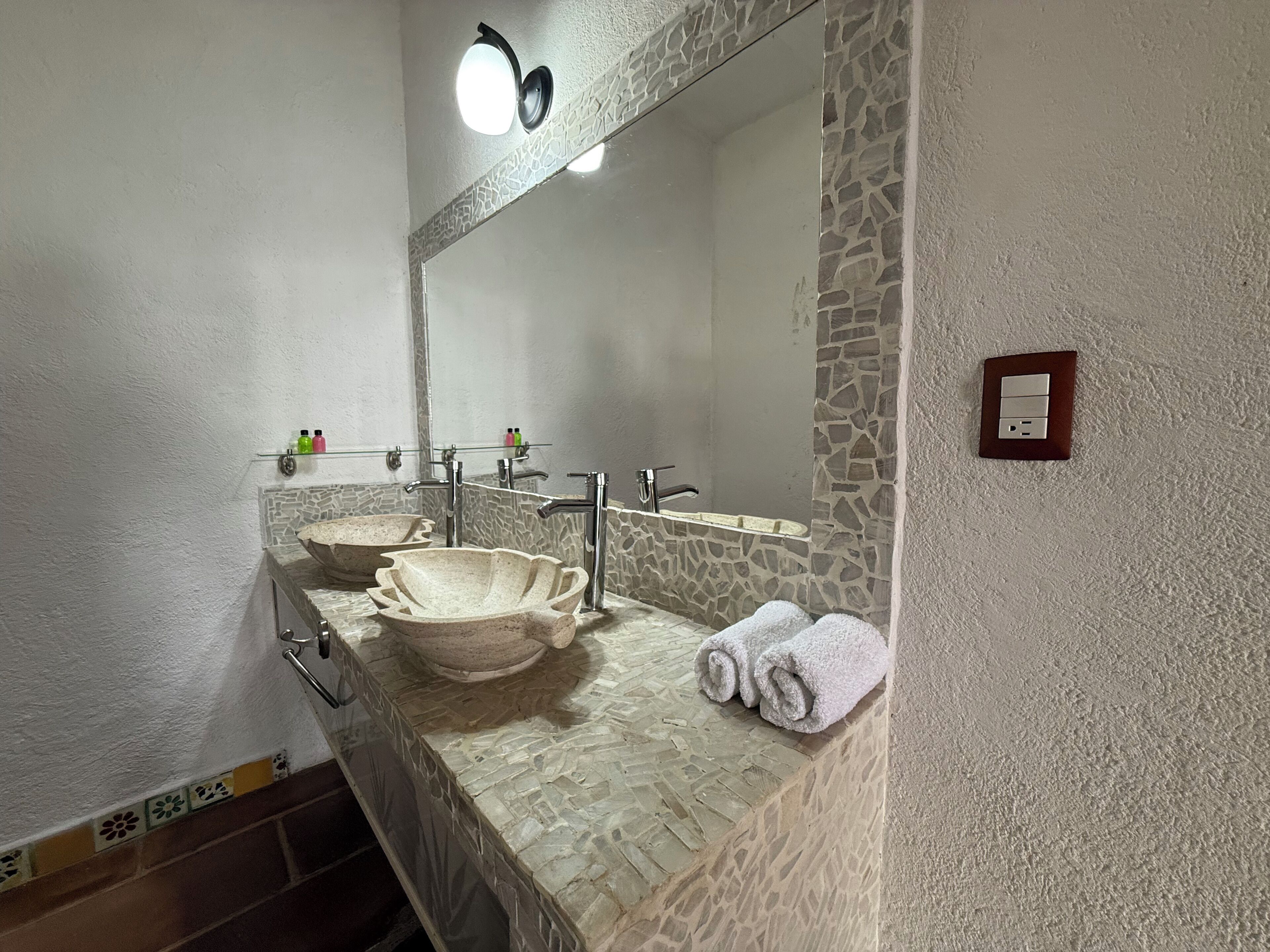 Une salle de bain avec un lavabo en pierre, un grand miroir et un porte-serviettes.