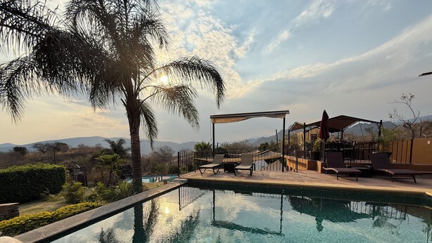 Ein klares Schwimmbecken mit Liegestühlen und einer Pergola, umgeben von Palmen und Blick auf Berge.