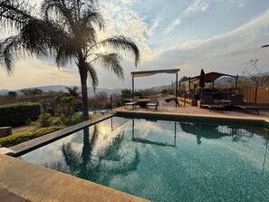 A clear swimming pool with lounge chairs and a pergola, surrounded by palm trees and a view of mountains. - Wellness Petfrendly El Secreto (Tepoztlan)