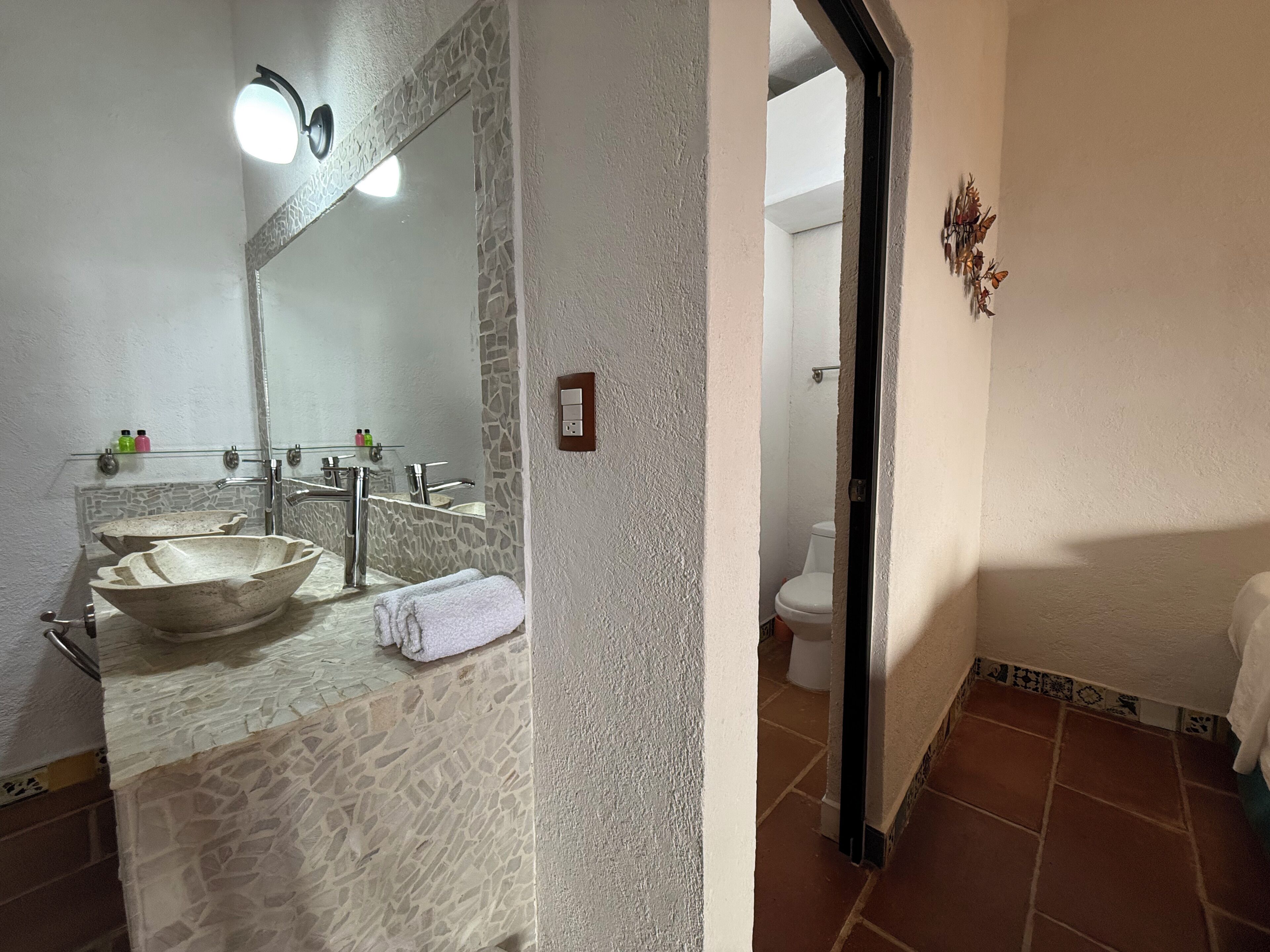 Un baño con un lavabo de piedra, un espejo, una toalla, un inodoro y una lámpara empotrada en la pared.