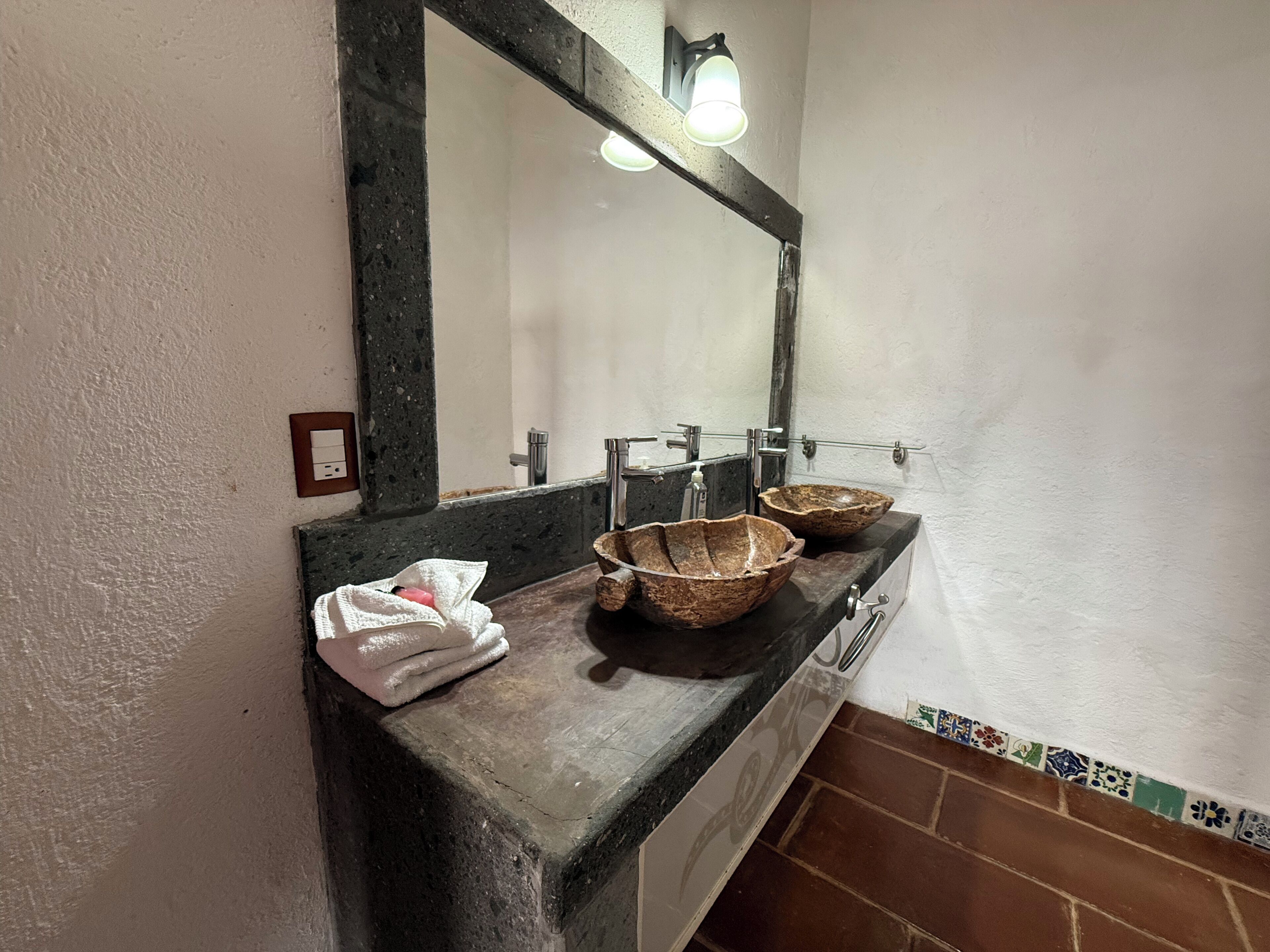 Un baño con tocador de madera, dos lavabos de piedra, un espejo y una toalla.