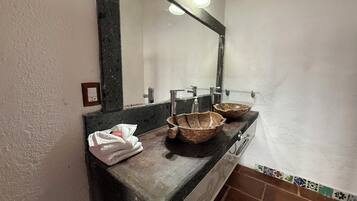 Un baño con tocador de madera, dos lavabos de piedra, un espejo y una toalla.