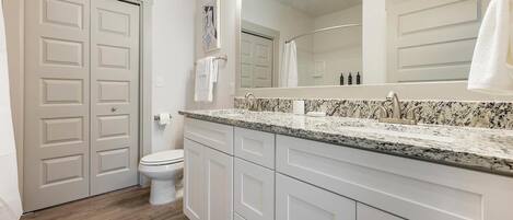 A bathroom with a toilet, a sink with a granite countertop, and a large mirror.