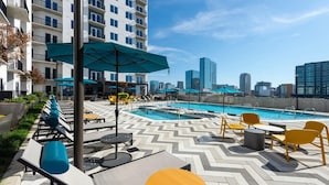 A rooftop pool area with lounge chairs, umbrellas, and a city skyline view. - Landing | Beautiful 1BD, Pool, Gym (Nashville)