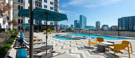 A rooftop pool area with lounge chairs, umbrellas, and a city skyline view.