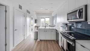 A modern kitchen with white cabinetry, a central island, a black tiled backsplash, and a built-in oven. - Landing | Beautiful 1BD, Pool, Gym (Nashville)