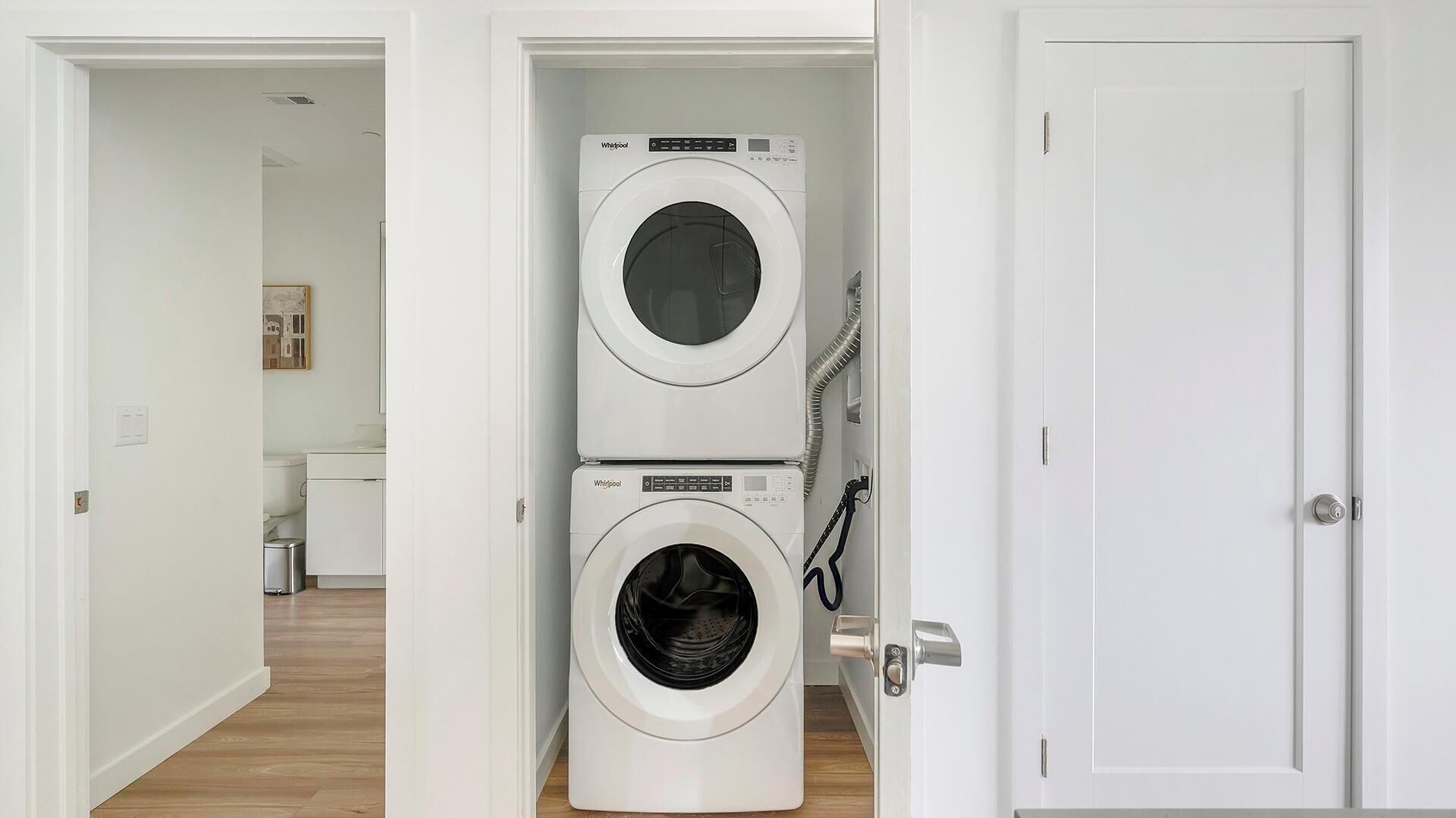 Pesuhuoneessa on kaksi päällekkäin asennettua Whirlpool-pyykinpesukonetta, ovi ja käytävä, joka johtaa kylpyhuoneeseen.
