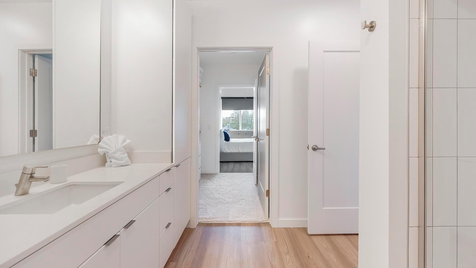 A modern bathroom with a large mirror, white cabinetry, and a white towel on the counter.