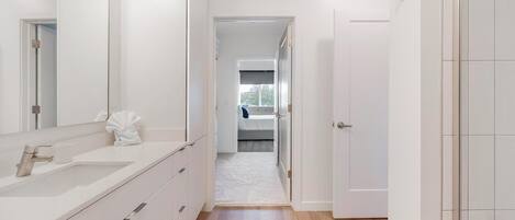A modern bathroom with a large mirror, white cabinetry, and a white towel on the counter.