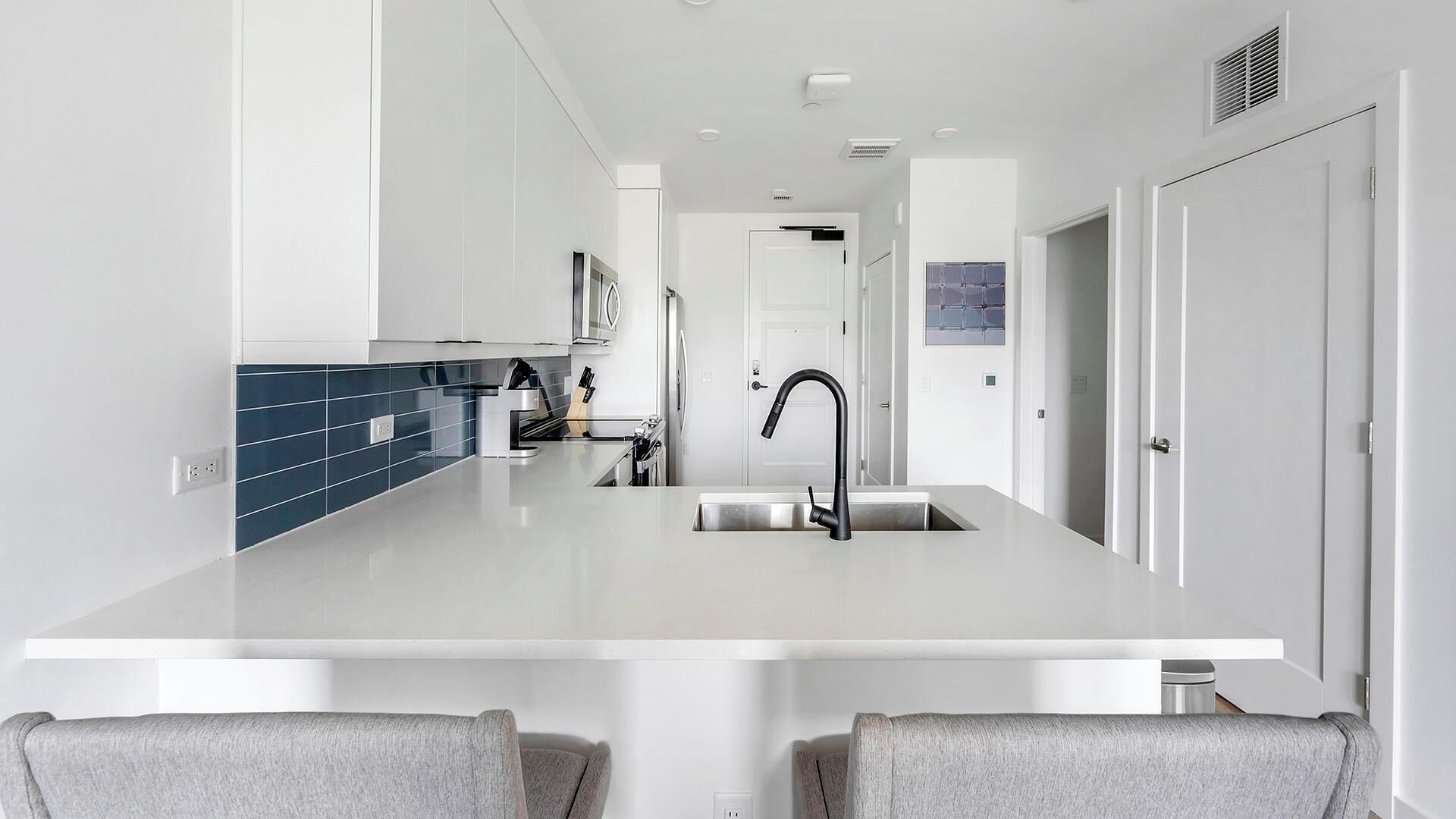 Una cocina moderna con una isla central, armarios blancos y un salpicadero azul.