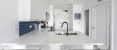 Una cocina moderna con una isla central, armarios blancos y un salpicadero azul.