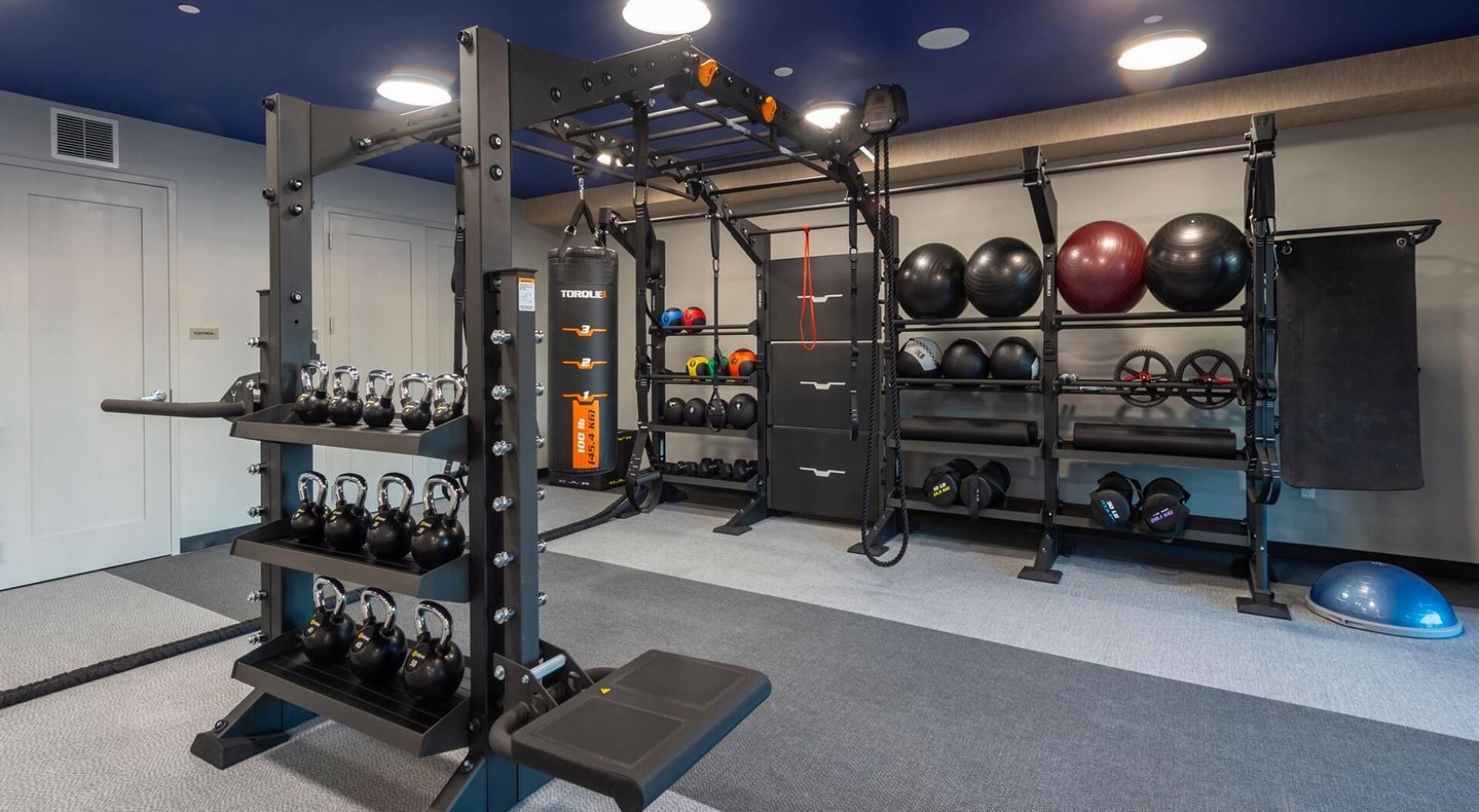 Une salle de sport à domicile équipée d’un support à squats, de kettlebells, d’un banc de développé couché et de divers poids.
