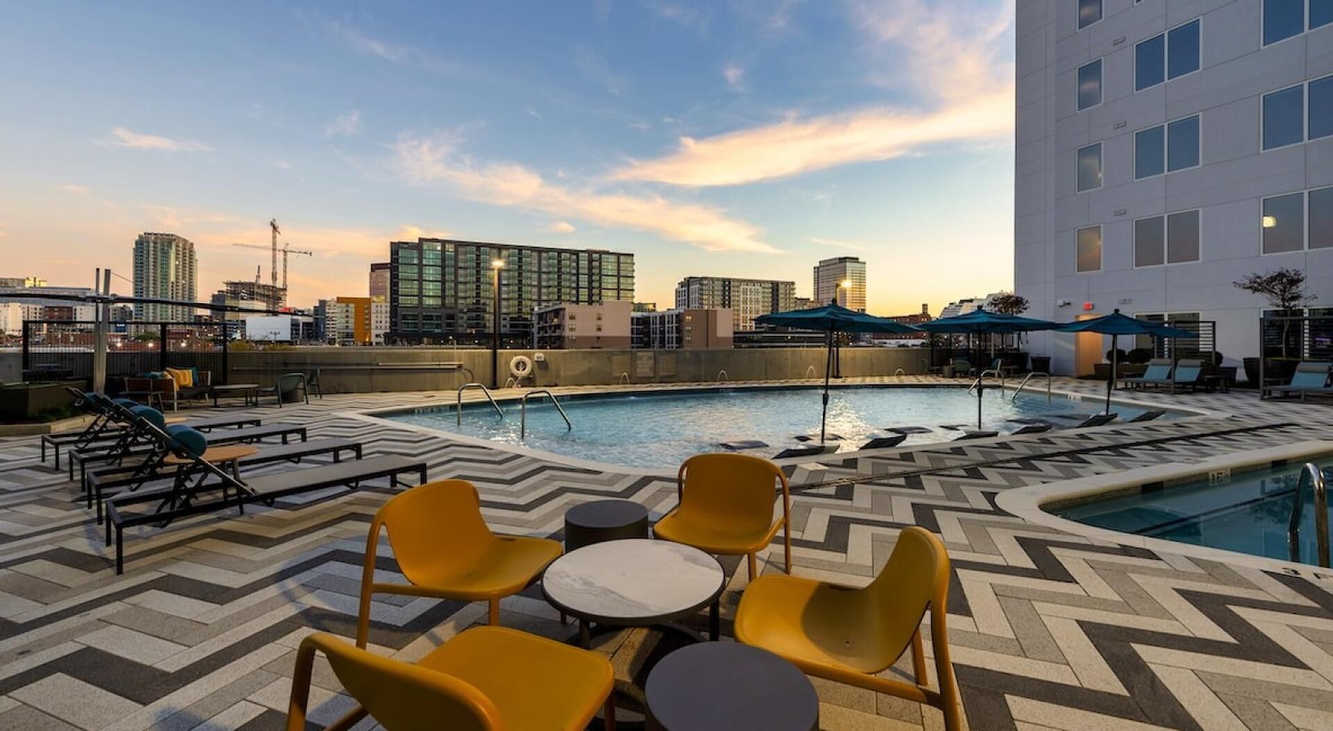 Un espace piscine aménagé sur le toit, avec des chaises longues et des tables, entouré d’immeubles de la ville.