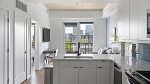 A modern kitchen with a central island, a dining area with a table and chairs, a built-in oven, and a view of the city through large windows. - Landing | Beautiful 1BD, Pool, Yoga Studio (Nashville)