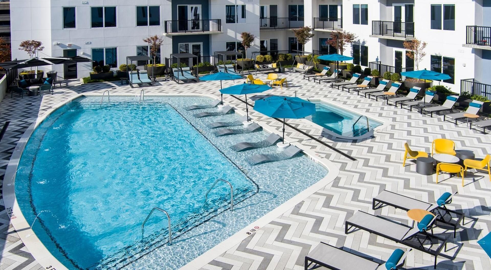 A rooftop pool area with multiple lounge chairs and umbrellas, surrounded by a white building with balconies.