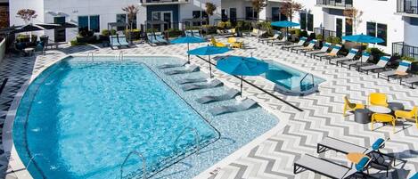 A rooftop pool area with multiple lounge chairs and umbrellas, surrounded by a white building with balconies.