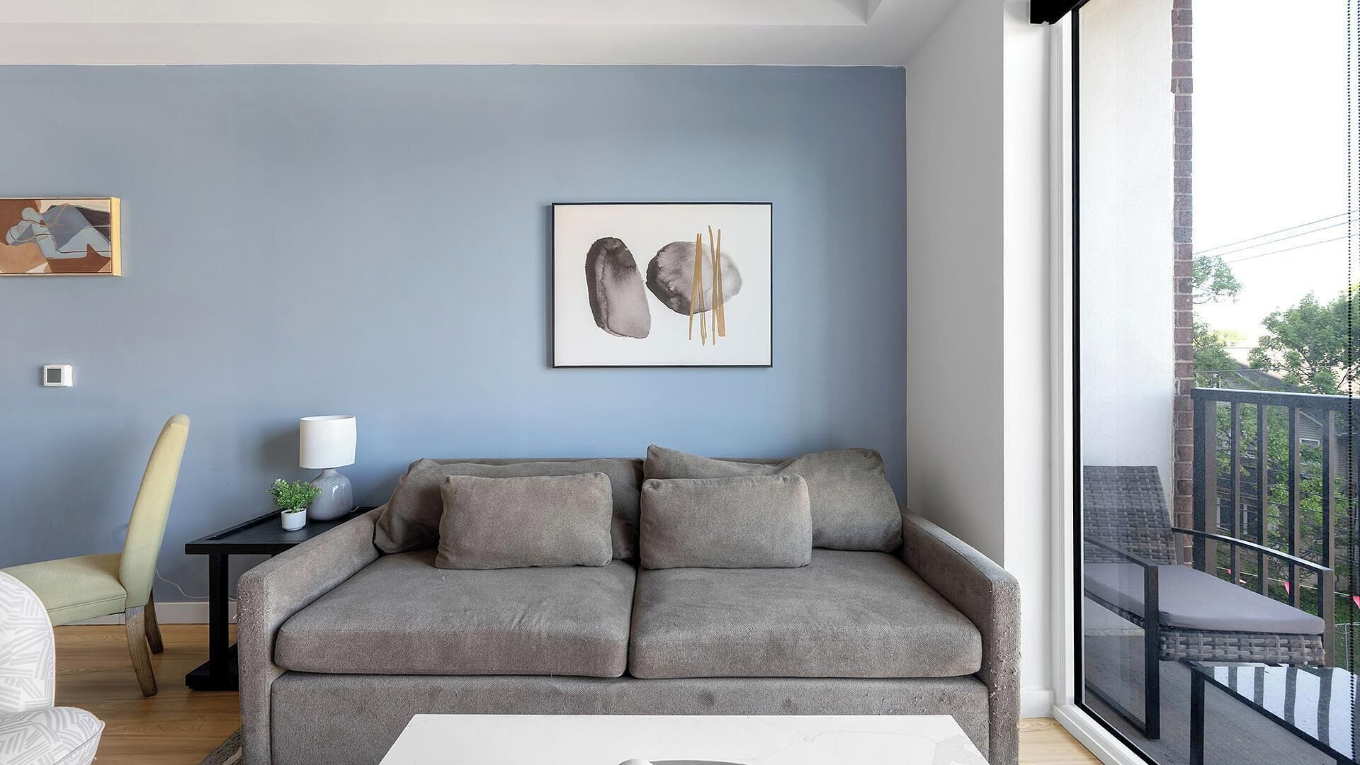 A modern living room with a grey sofa, a small side table with a lamp, and a framed abstract painting on the wall.