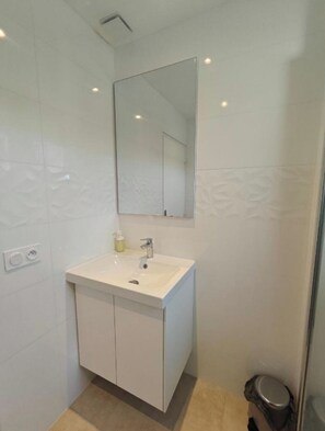 Une salle de bain moderne avec un meuble-lavabo blanc, un miroir et un espace douche.