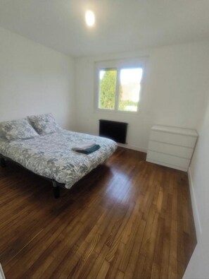 Une chambre à coucher avec un lit, une fenêtre, un radiateur et une commode blanche.