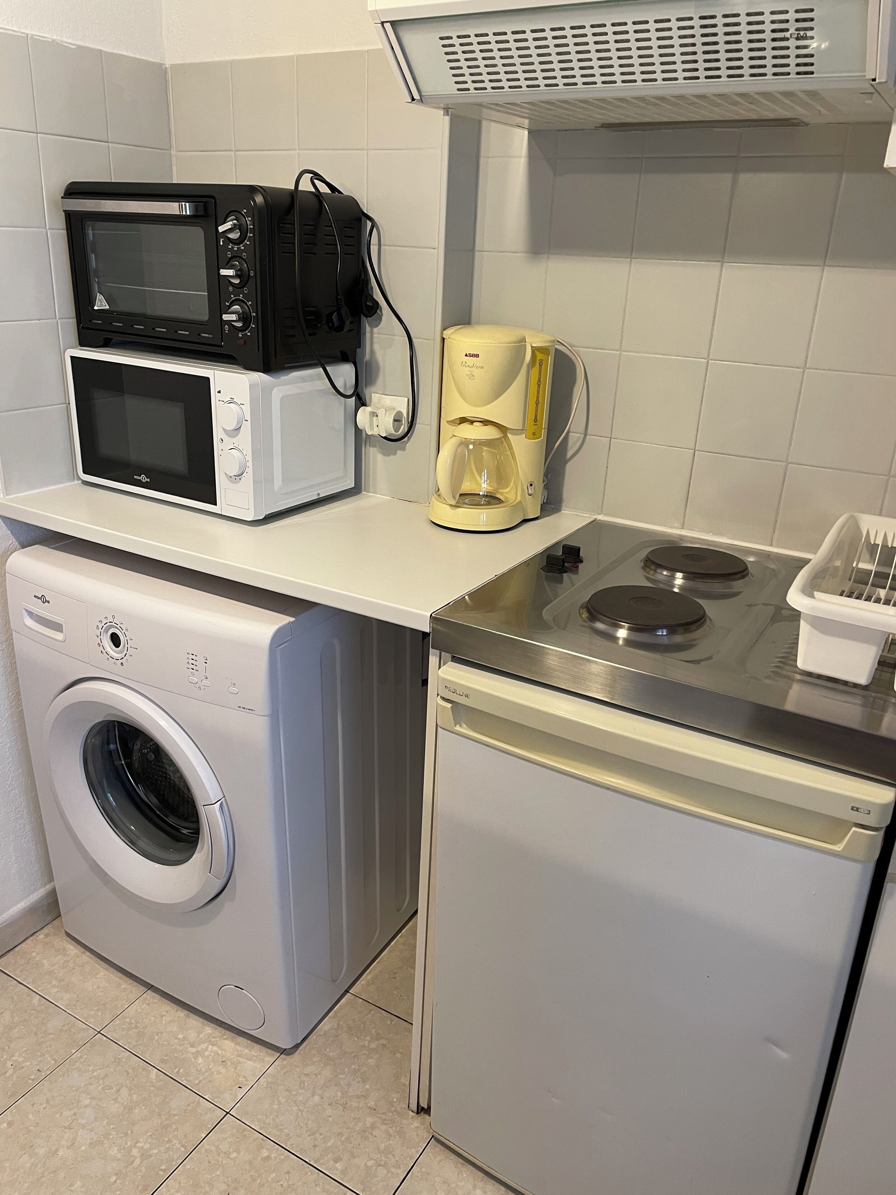 A compact kitchen with a washing machine, microwave, coffee maker, and a small stove.