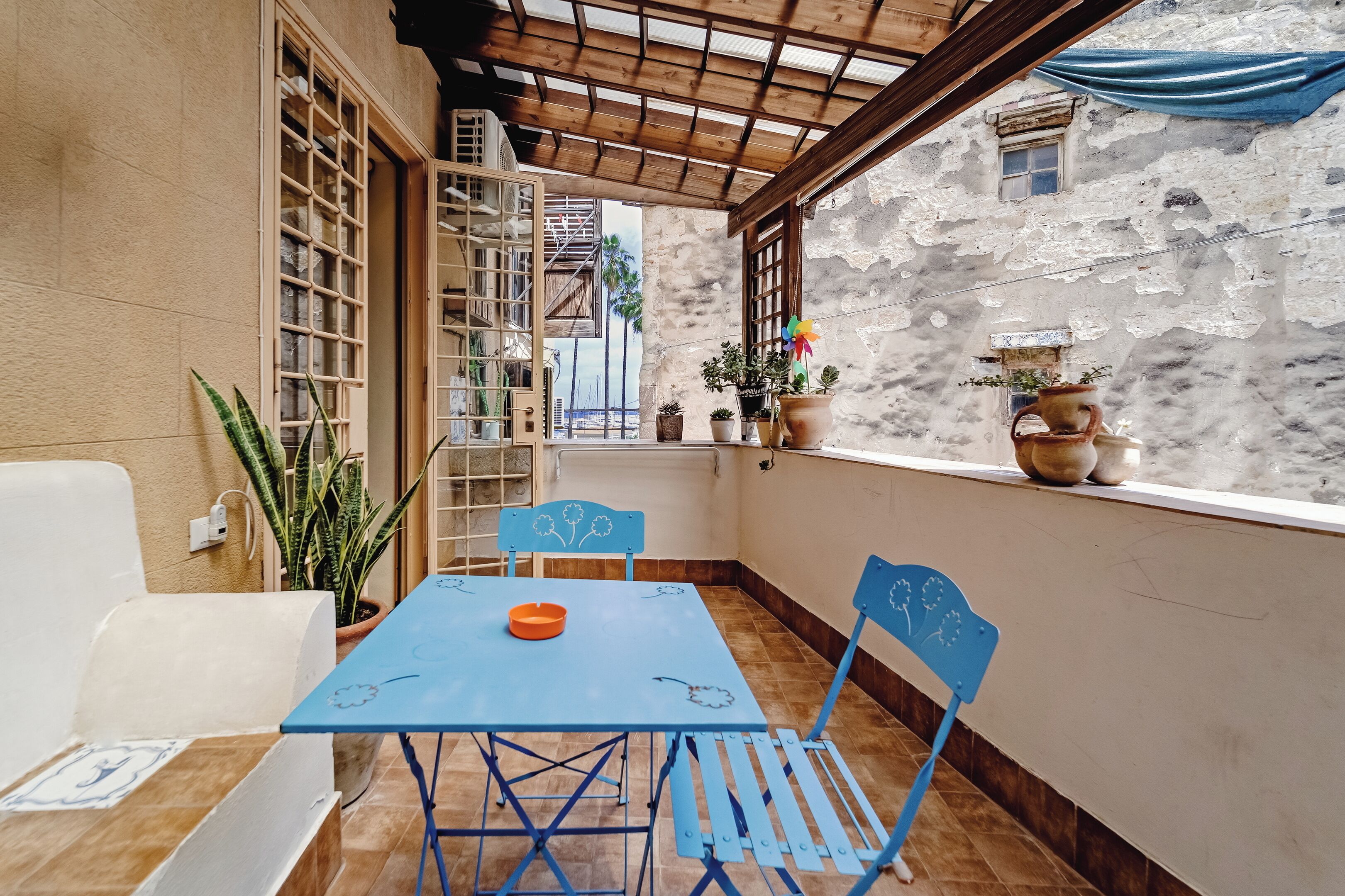 Une petite terrasse avec une table et des chaises bleues, des plantes en pot et une vue sur un bâtiment historique.