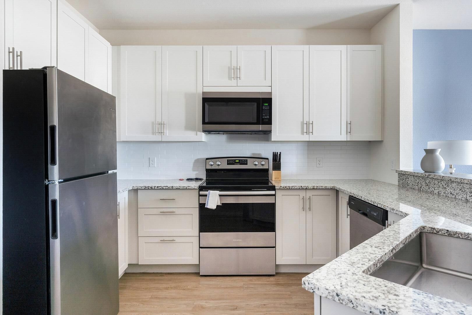 A modern kitchen with white cabinets, a stainless steel refrigerator, a microwave, an oven, and a dishwasher.