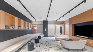 Ein modernes Wohnzimmer mit einer Couch, zwei Sesseln, einem Couchtisch und einem an der Wand montierten Flachbildfernseher.