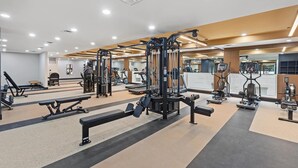Ein Fitnessraum mit unterschiedlichen Trainingsgeräten, einer Hantelbank und einer Spiegelwand.