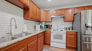 A kitchen with wooden cabinets, a white stove, a microwave, and stainless steel appliances. - Peaceful 3-bedroom house with AC in charming Kingston (Kingston)