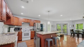 A modern kitchen with wooden cabinets, stainless steel appliances, a granite countertop, and a dining area with a table and chairs. - Peaceful 3-bedroom house with AC in charming Kingston (Kingston)