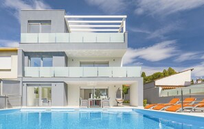 Um edifício moderno de dois andares com piscina, área de estar externa e céu claro.