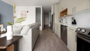 A modern kitchen with white cabinets, stainless steel appliances, and a grey sofa in the living area. - Landing | Amazing 1BD, Pool, Gym (Hyattsville)