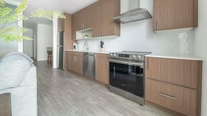 A modern kitchen with wooden cabinets, stainless steel appliances, and a white tiled backsplash. - Landing | Amazing 1BD, Game Room, Gym (Hyattsville)