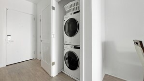 Uma lavanderia com duas máquinas de lavar empilhadas, uma porta e piso de madeira.
