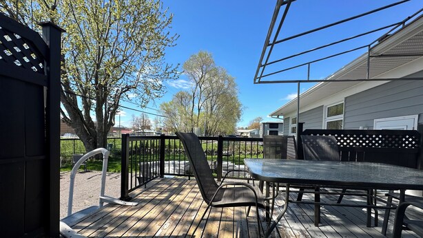 A wooden deck with a table and chairs, surrounded by a black metal fence, and trees in the background. - Large house with terrace+BBQ close to everything (Québec)
